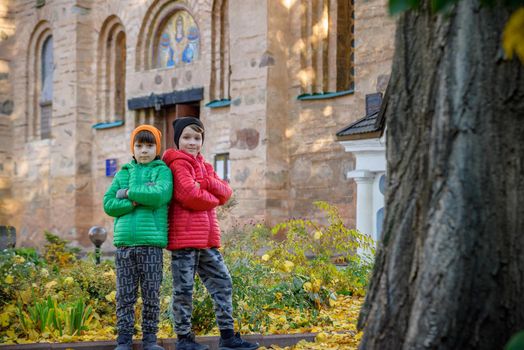 Young brothers near an ancient stone church. Kids smiling and happy having leisure time on autumn holiday. Travel with children concept.