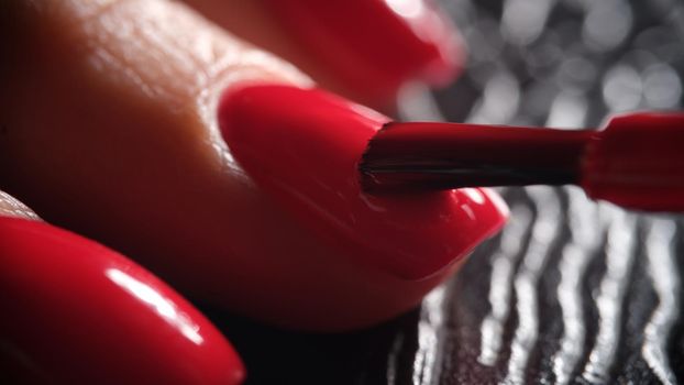 Master manicurist applies decorative bright red varnish on nail plate with brush. Concept of beauty and nail care