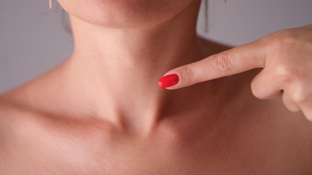Young woman pointing her finger at neck. Thyroid disease concept