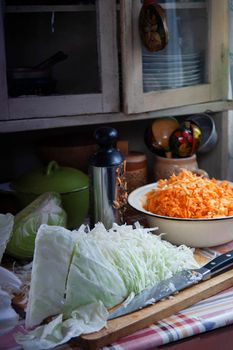 Cut cabbage and grated carrot prepared for home made cabbage sauerkrauting in old farm kitchen, selective focus.