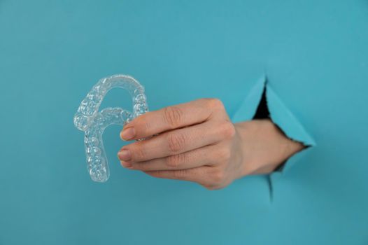 A female hand sticking out of a hole from a blue background holds removable night retainers