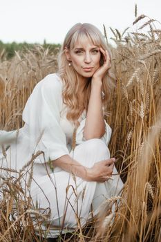 A blonde woman in a long white dress walks in a wheat field. The concept of a wedding and walking in nature.