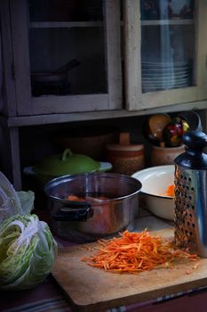 Grated carrot on wooden kitchen board prepared for cabbage sauerkrauting in old rustic kitchen, selective focus.