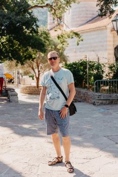 A handsome young man standing and smiling happily in the background of urban buildings. Forty years old caucasian tourist man outdoor near old city buildings - summer holiday.