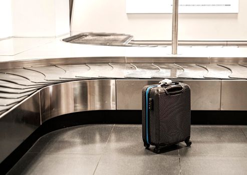 Black suitcase next to the baggage conveyor belt at the airport.