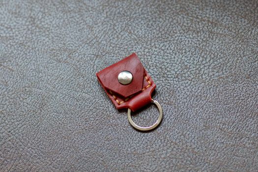 Orange leather key strap with iron ring for mounting on a belt on a leather background. Back side.