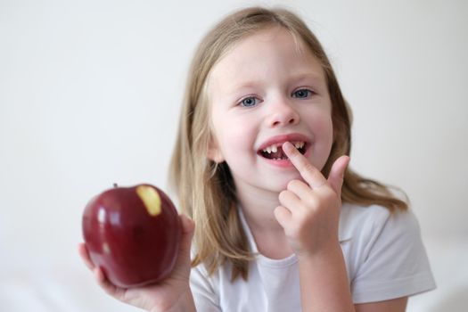 Portrait of smiling cute girl without teeth with red bitten apple in hand. Healthy baby teeth concept