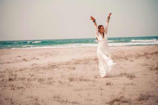 Model in boho style in a white long dress and silver jewelry on the beach. Her hair is braided, and there are many bracelets on her arms