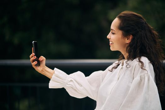 Profile of a curly brunette girl taking a selfie in the park. High quality photo