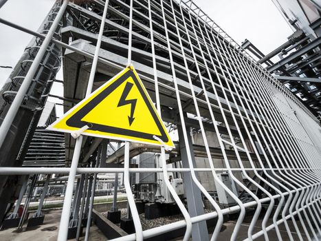 Danger Sign High voltage in the yellow triangle on the metal fence of the grid