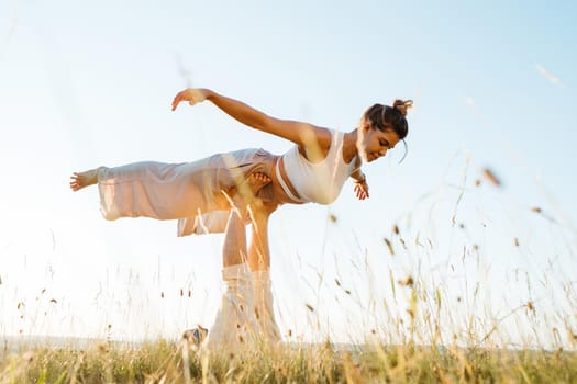 Couple Making Beautiful Pose, Man and Woman Practicing Yoga Outdoors at Sunset with Sky on Background