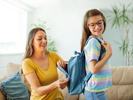 Mother helping daughter to get ready for school, helping her with backpack and books,hugging and leaving home