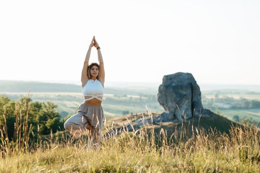 Young Woman Meditating and Practicing Yoga Outdoors at Sunset with Scenic Landscape and Nature Miracle Giant Stone on Background