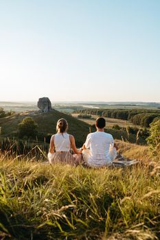 Man and Woman Practicing Yoga and Meditation Outdoors at Sunset with Scenic Landscape and Nature Miracle Giant Stone on Background