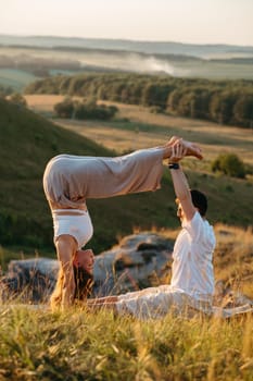 Young Adult Couple, Man and Woman Practicing Yoga Outdoors at Sunset with Scenic Landscape on Background