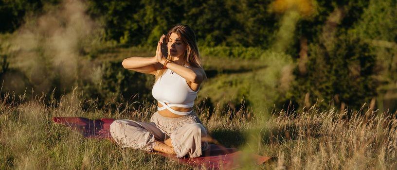 Young Woman Practicing Yoga and Meditation on the Mat Outdoors at Sunset with Beautiful Landscape on Background