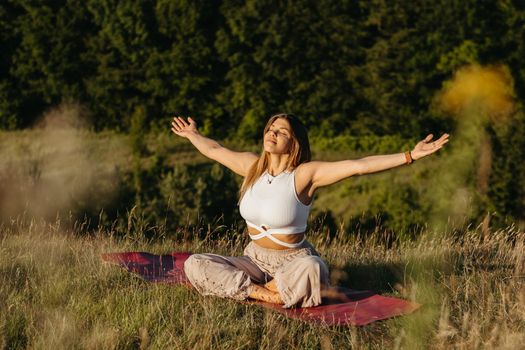 Young Woman Sunbathing and Meditating on the Mat Outdoors at Sunset with Beautiful Landscape on Background