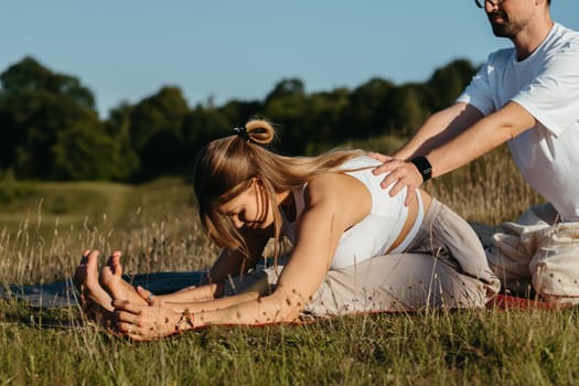 Man Helping Woman Doing Stretching Outdoors, Young Adult Couple Practicing Yoga