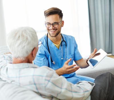 Doctor or nurse caregiver helping senior man with a tablet at home or nursing home