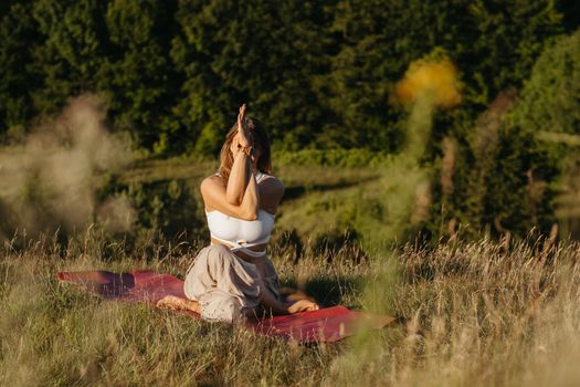 Young Woman Practicing Yoga on the Mat Outdoors at Sunset with Beautiful Landscape on Background