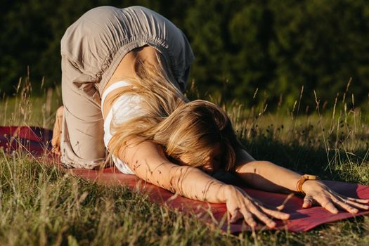 Young Woman Doing Puppy Dog Yoga Pose on Mat Outdoors at Sunset