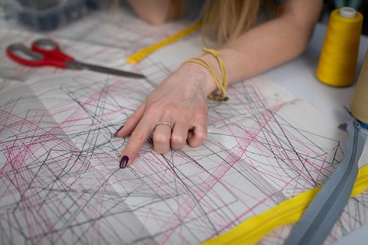 A woman's index finger shows lines in a sundry paper pattern. A tailor's workshop up close.