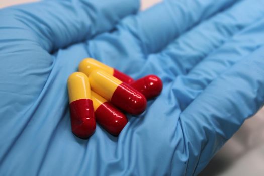 Yellow-red capsules with medicine close-up in the hand of a doctor in a blue medical glove.