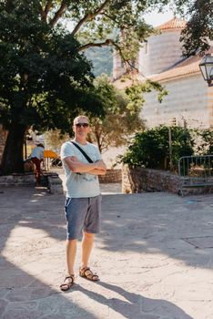 A handsome young man standing and smiling happily in the background of urban buildings. Forty years old caucasian tourist man outdoor near old city buildings - summer holiday.