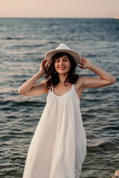 A woman in a white dress and hat is standing on the beach enjoying the sea. Happy summer holidays.