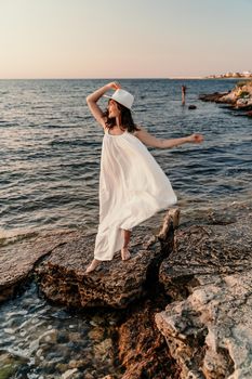 A woman in a white dress and hat is standing on the beach enjoying the sea. Happy summer holidays.