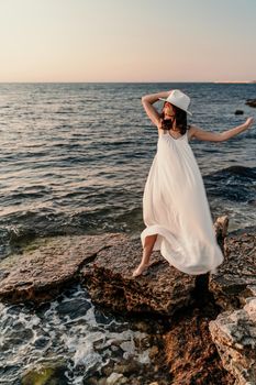 A woman in a white dress and hat is standing on the beach enjoying the sea. Happy summer holidays.