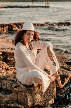 A woman in a white pantsuit and hat is standing on the beach enjoying the sea. Happy summer holidays.