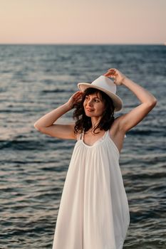 A woman in a white dress and hat is standing on the beach enjoying the sea. Happy summer holidays.