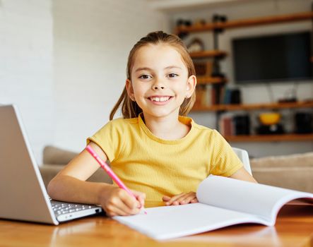 Portrait of a little girl having fun using laptop or doing homework with laptop at home