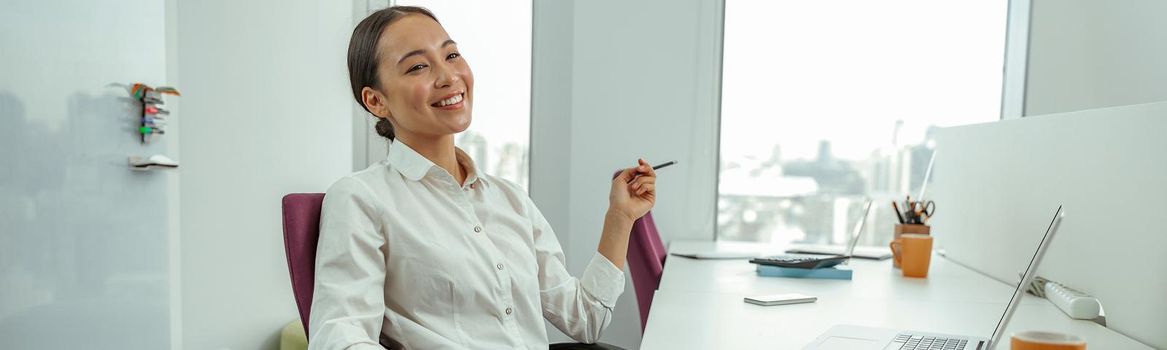 Smiling asian business woman sitting in office on her workplace and looks away. High quality photo