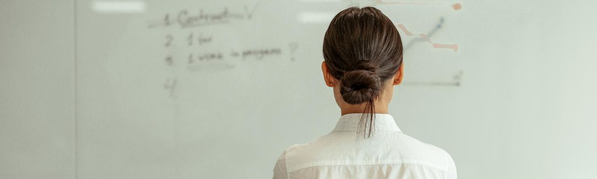 Business woman looks at flipboard with charts and plans in office. View from the back