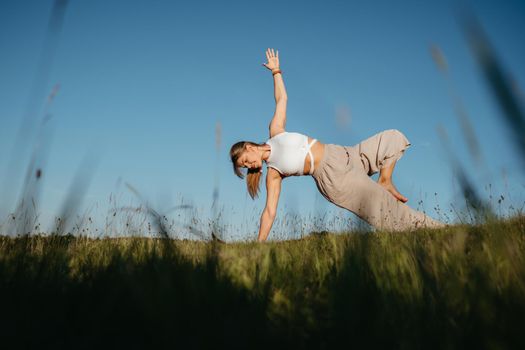 Young Woman Practicing Yoga Outdoors in the Field with Blue Sky on Background