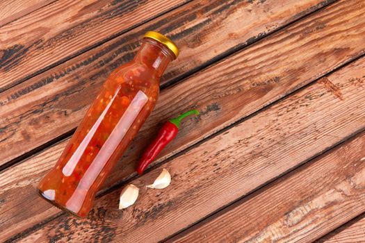 Bottle of spicy red hot sauce on wooden background