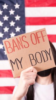 Young woman holding sign Bans Of My Body covering face stop abortion American flag on background. Anti domestic violence, racism racial discrimination. Struggle for women rights, social problems