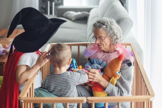 Gray-haired grandmother plays with her little grandchildren in a flat