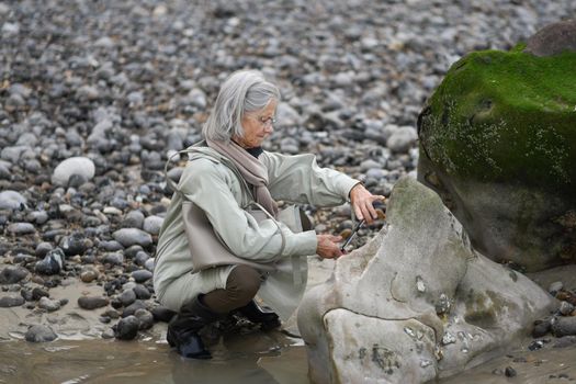 Gray-haired woman makes photo on smartphone at the ocean