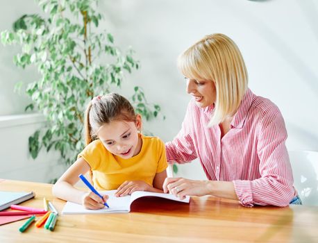 mother or teacher teaching daughter and helping her with homework at home or in classroom