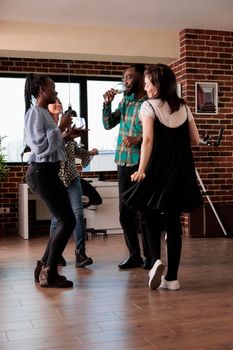 Multiethnic group of close friends dancing at party while celebrating important event. Happy diverse people listening to funky disco music while drinking wine and having fun time together.