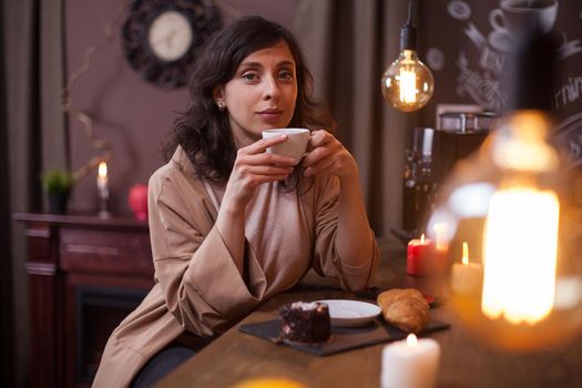 Attractive girl drinking delicious coffee and looking at the camera in a coffee bar, Beautiful young woman in a coffee bar holding a coffee cup.