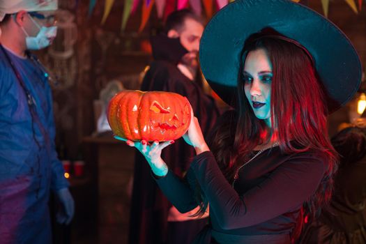 Portrait of beautiful woman dressed up like a witch doing dark magic on a pumpkin for halloween. Dracula at halloween party.