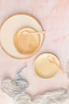 Areca leaf plates with recyclable spoons on a pink marble kitchen counter. Healthy food concept with environmental sustainability concerns.