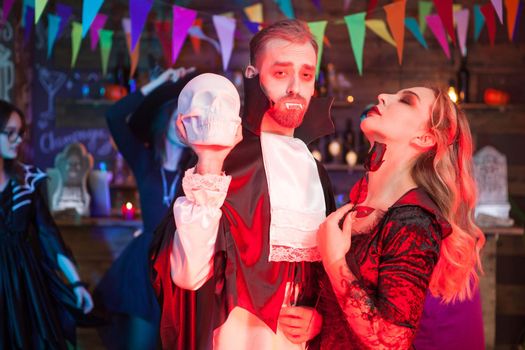 Beautiful couple dressed up like Dracula and a sexy witch for halloween party. Dracula holding a scary skull.