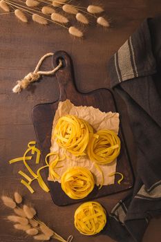 Tagliatelle noodles pasta in wooden cutting board on rustic kitchen countertop.