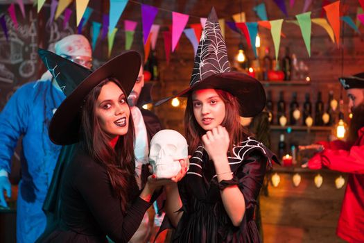 Beautiful young witches with big hats celebrating halloween. Scary doctor in the background.