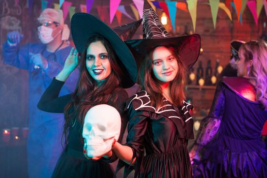 Sisters dressed up like witches at a halloween party holding a skull. Witches gathering. Halloween costume.